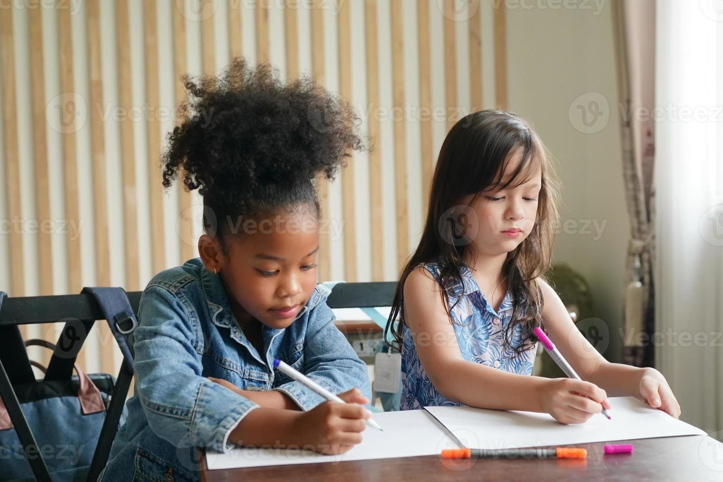 Preschool Girl Kid Drawing With Color Pencil On White Paper On Table In Classroom With Friends photo