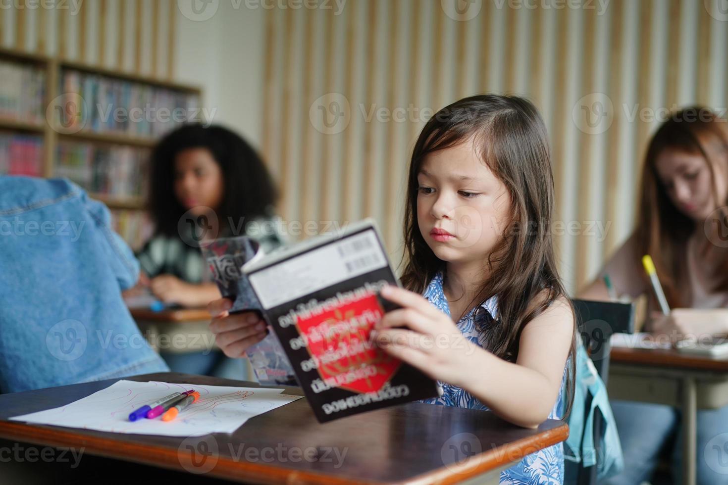 Preschool Girl Kid Drawing With Color Pencil On White Paper On Table In Classroom With Friends photo