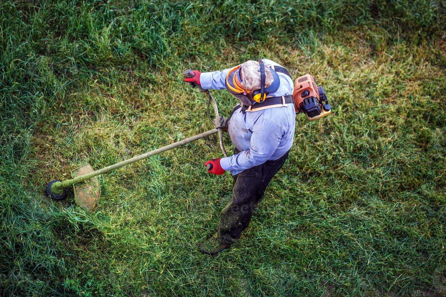 Top view fat dirty lawnmover man worker cutting dry grass with lawn mower. photo
