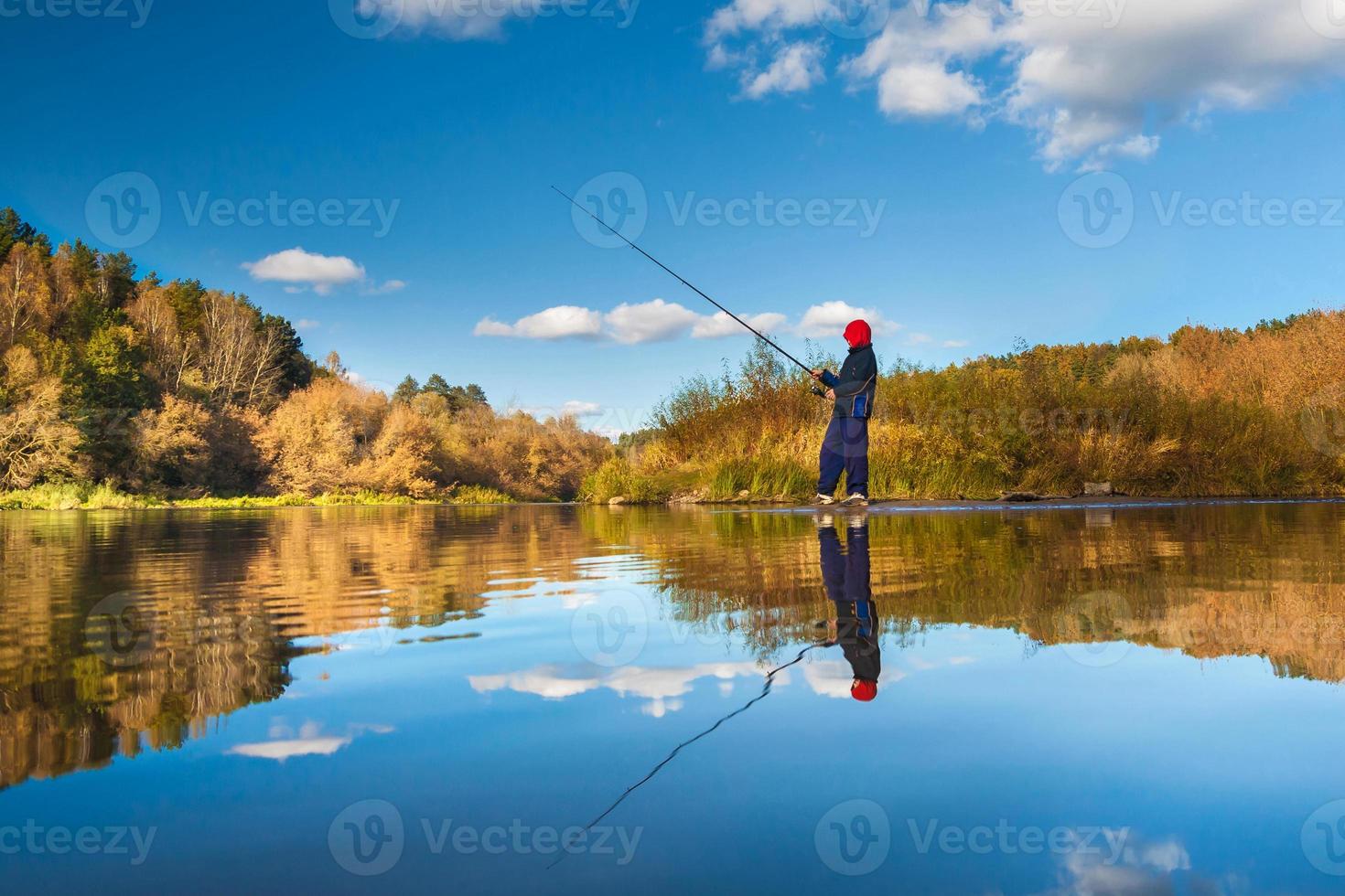 Fisherman boy on panoramic landscape with wide broad river in autumn forest in sunny day with reflection photo