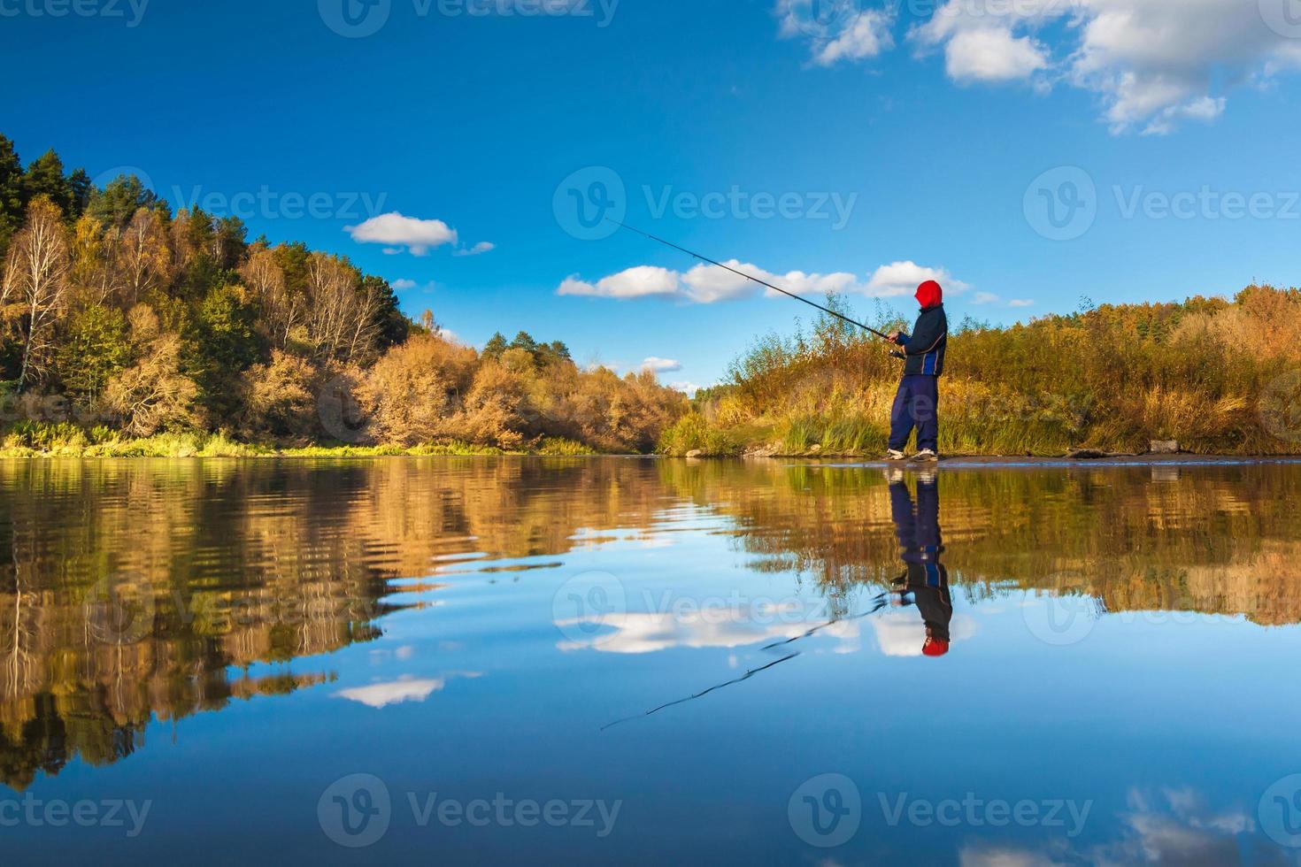 Fisherman boy on panoramic landscape with wide broad river in autumn forest in sunny day with reflection photo