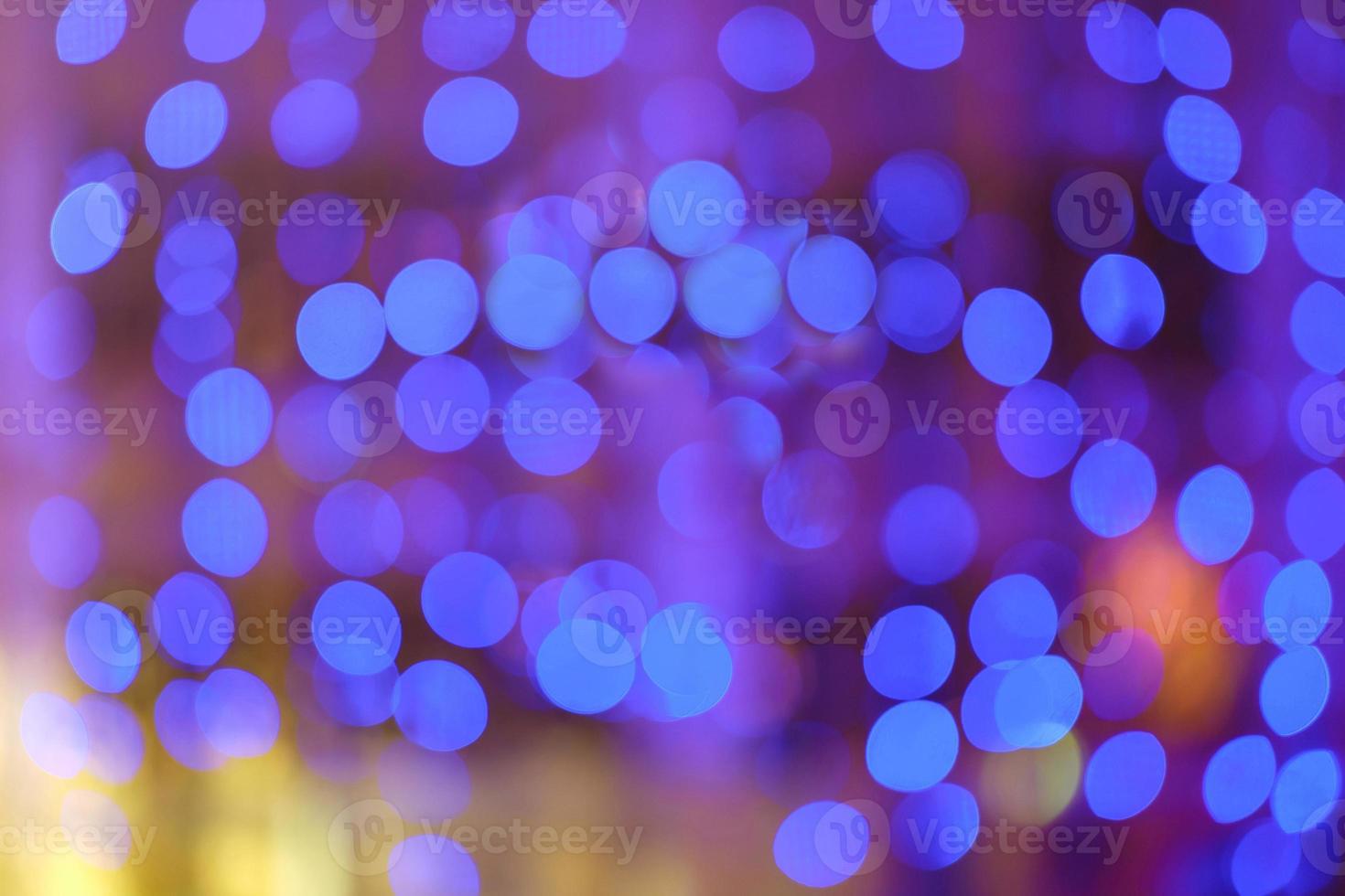 Blurred bokeh colorful lights lanterns, holiday new year lighting on black background Christmas winter glitter shiny light bokeh in rainbow colors. Holiday purple blue pink violet natural texture. photo