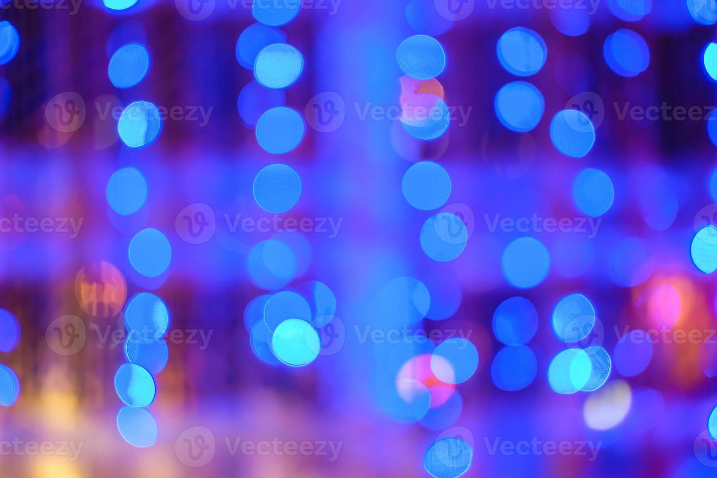 Blurred bokeh colorful lights lanterns, holiday new year lighting on black background Christmas winter glitter shiny light bokeh in rainbow colors. Holiday purple blue pink violet natural texture. photo