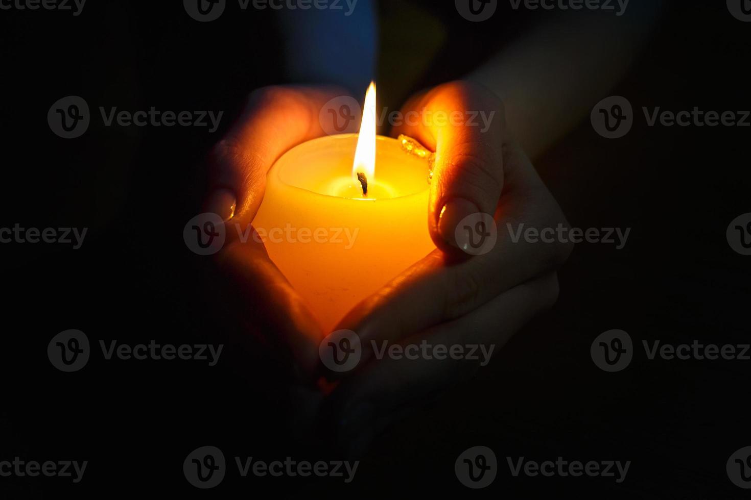 vela encendida en manos de una niña rezando sobre un fondo negro foto