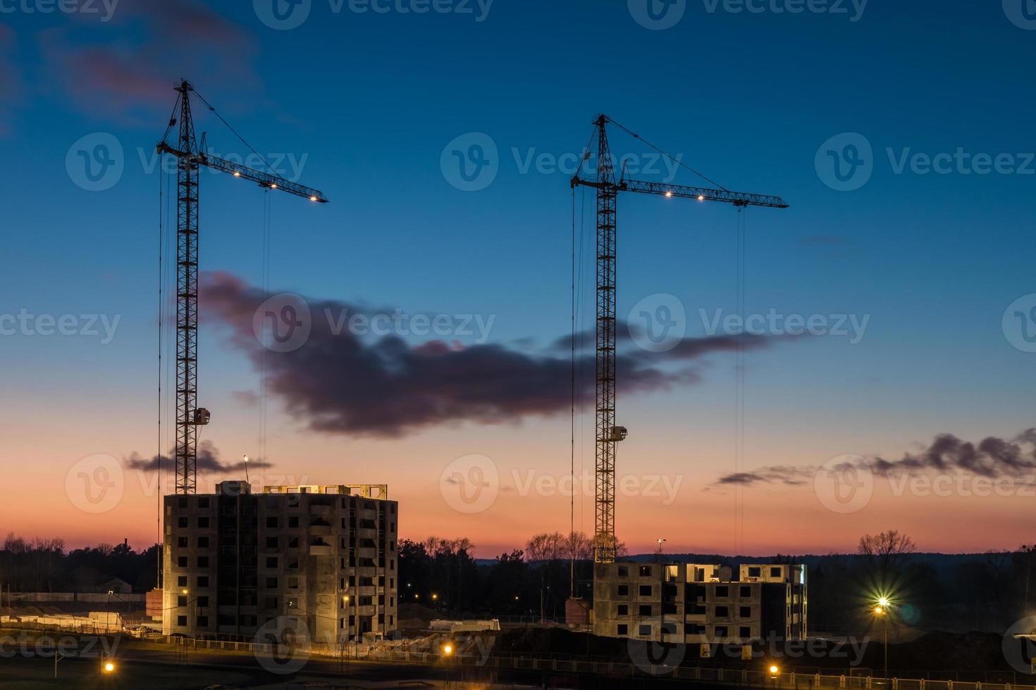 Tower cranes and unfinished multi-storey high near buildings under construction site in the sunset evening with dramatic colorful cloud background photo