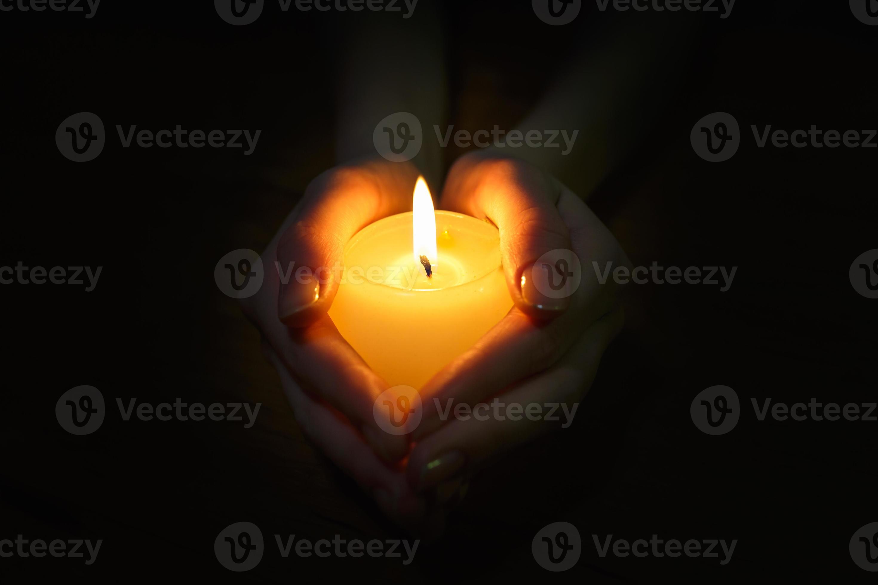 burning candle in the hands of a praying girl on a black background
