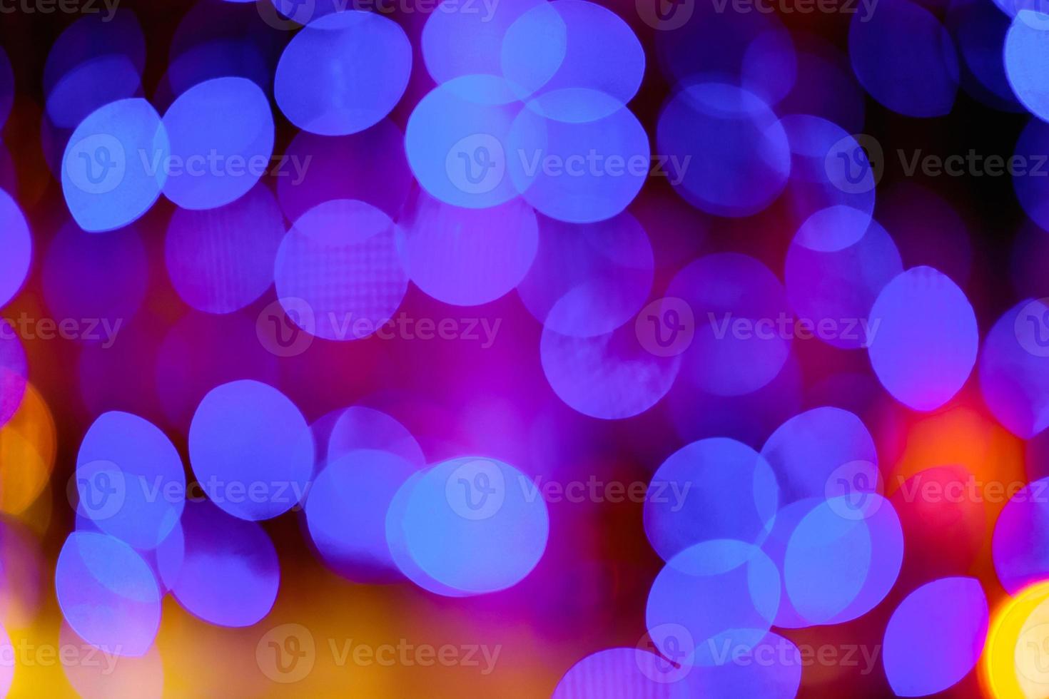 Blurred bokeh colorful lights lanterns, holiday new year lighting on black background Christmas winter glitter shiny light bokeh in rainbow colors. Holiday purple blue pink violet natural texture. photo