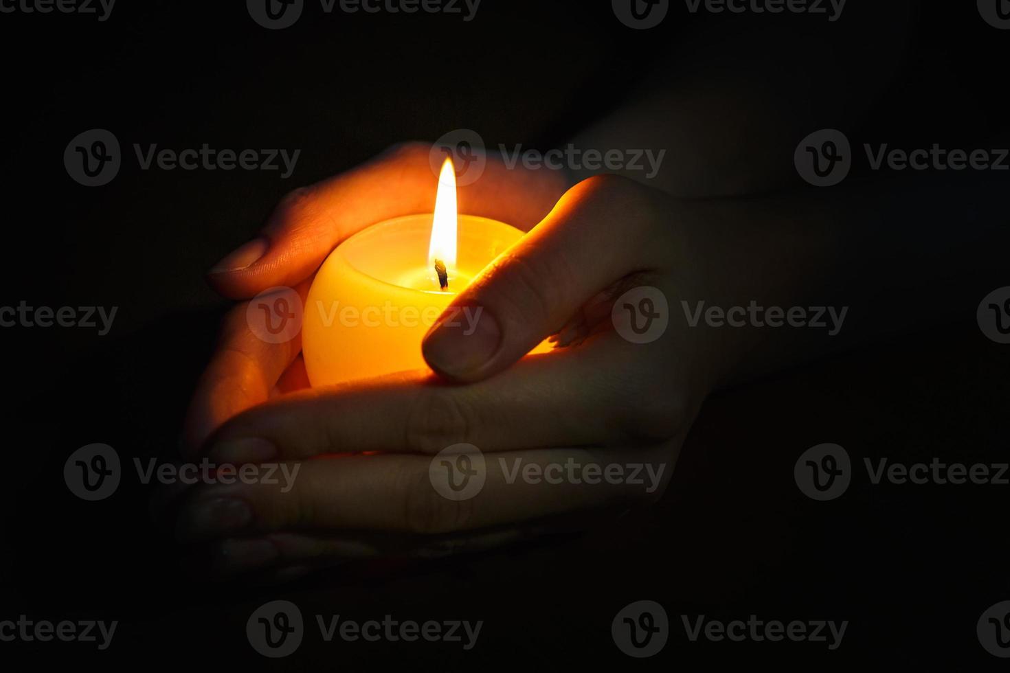 burning candle in the hands of a praying girl on a black background photo