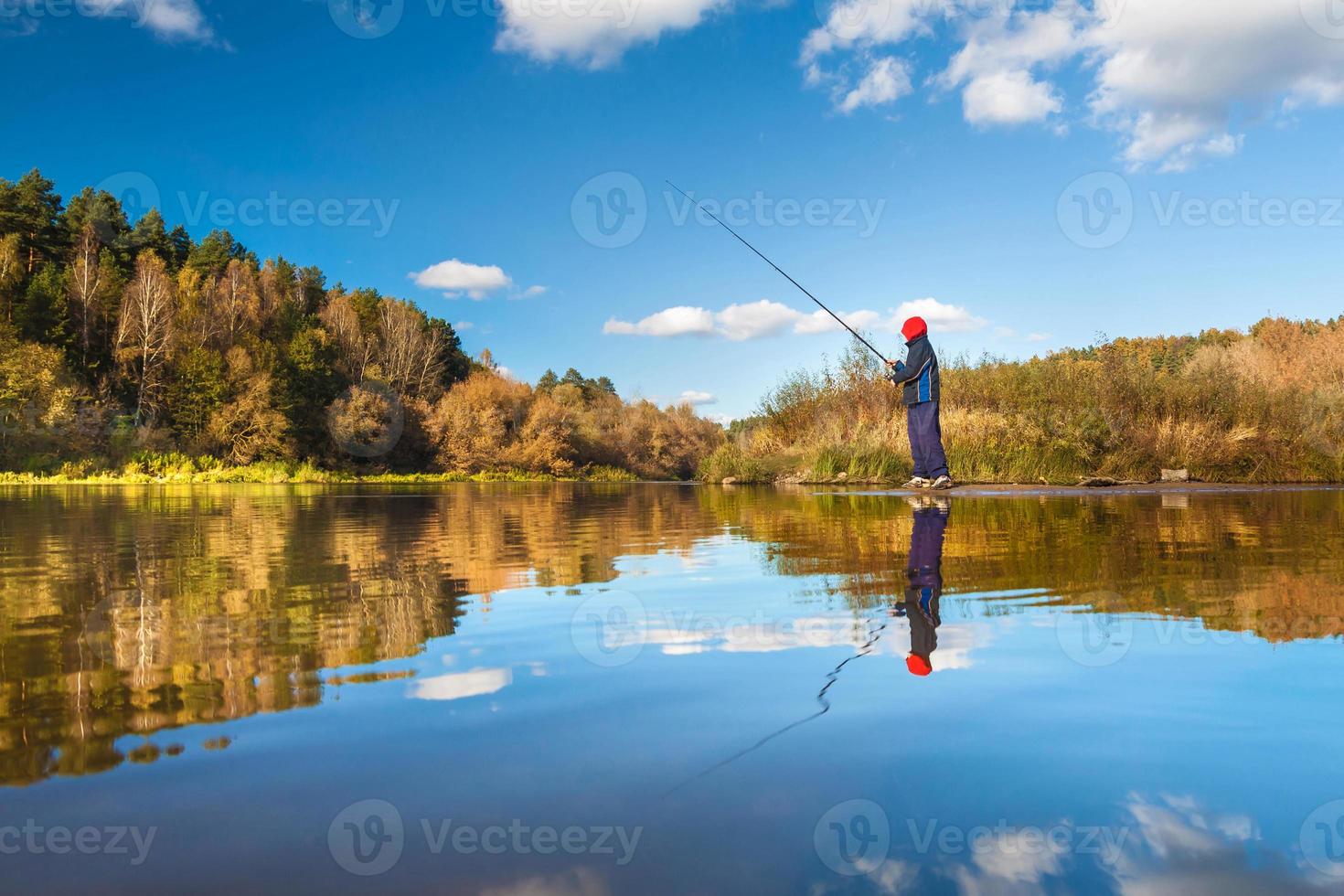 Fisherman boy on panoramic landscape with wide broad river in autumn forest in sunny day with reflection photo