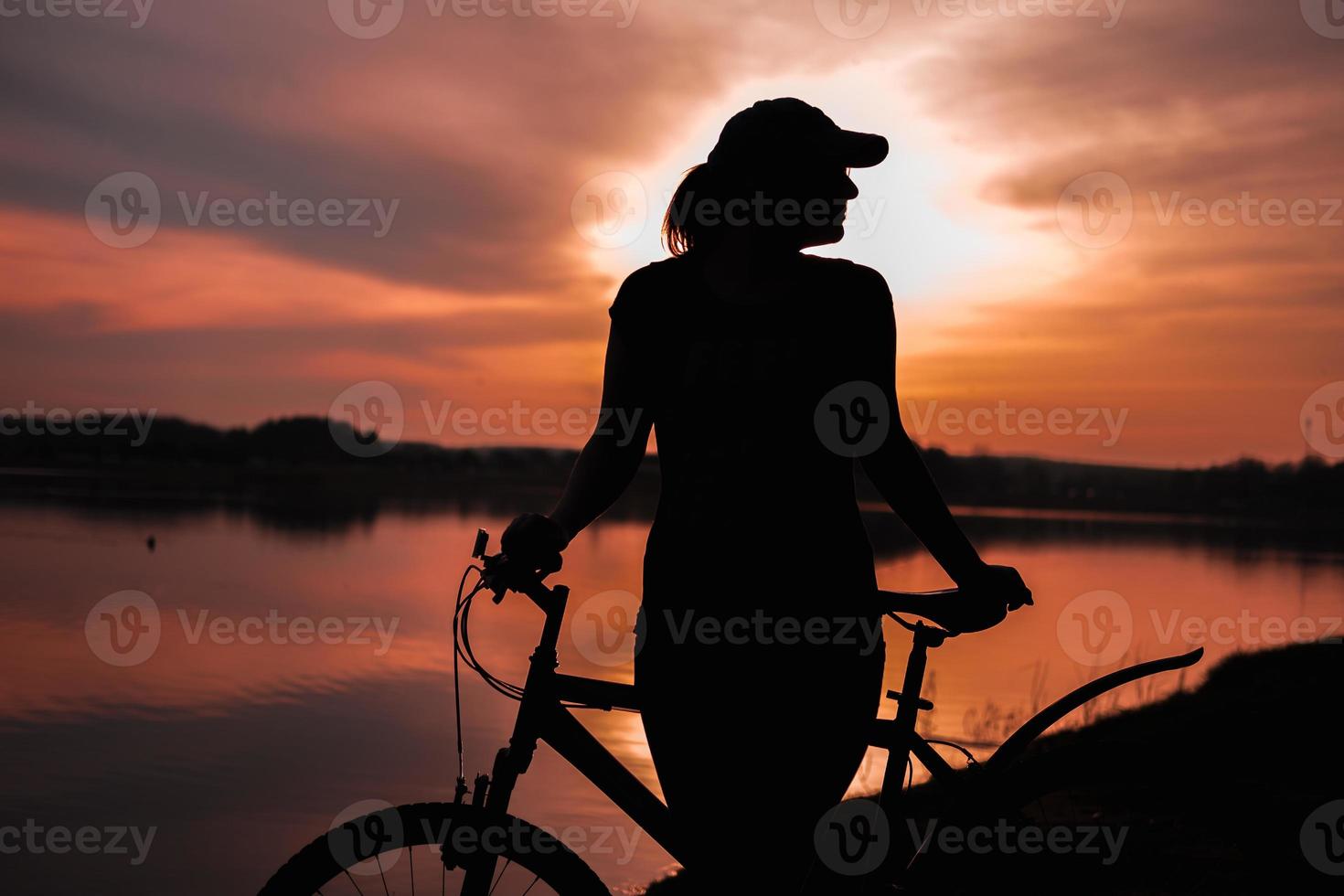 Summer silhouette landscape. Girl with a bicycle by the lake against the backdrop of the setting sun, the crimson sunset photo