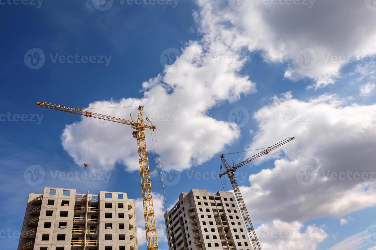 Tower cranes and unfinished multi-storey high near buildings under construction site in the sunny day with beautiful clouds photo
