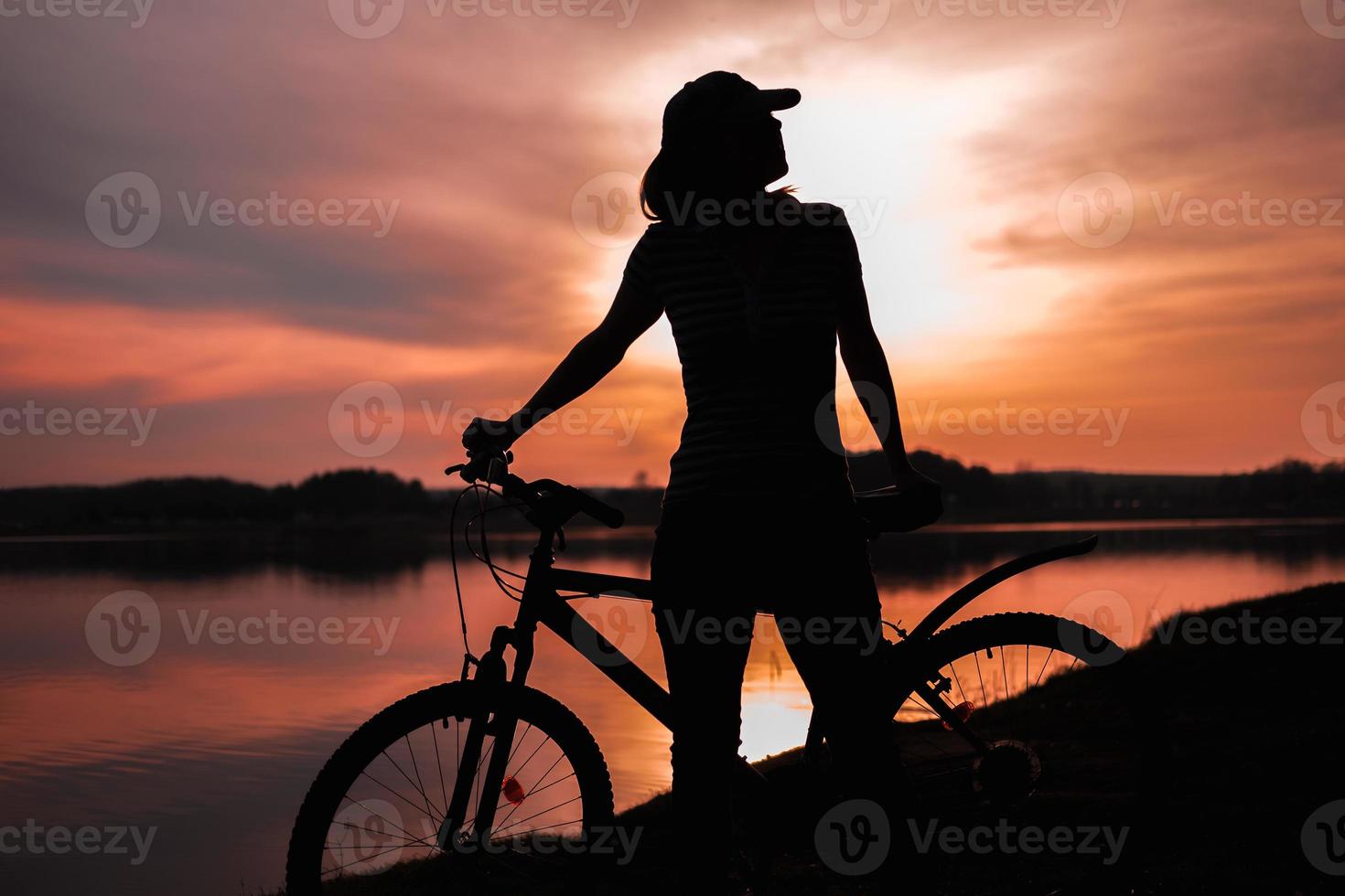 Summer silhouette landscape. Girl with a bicycle by the lake against the backdrop of the setting sun, the crimson sunset photo
