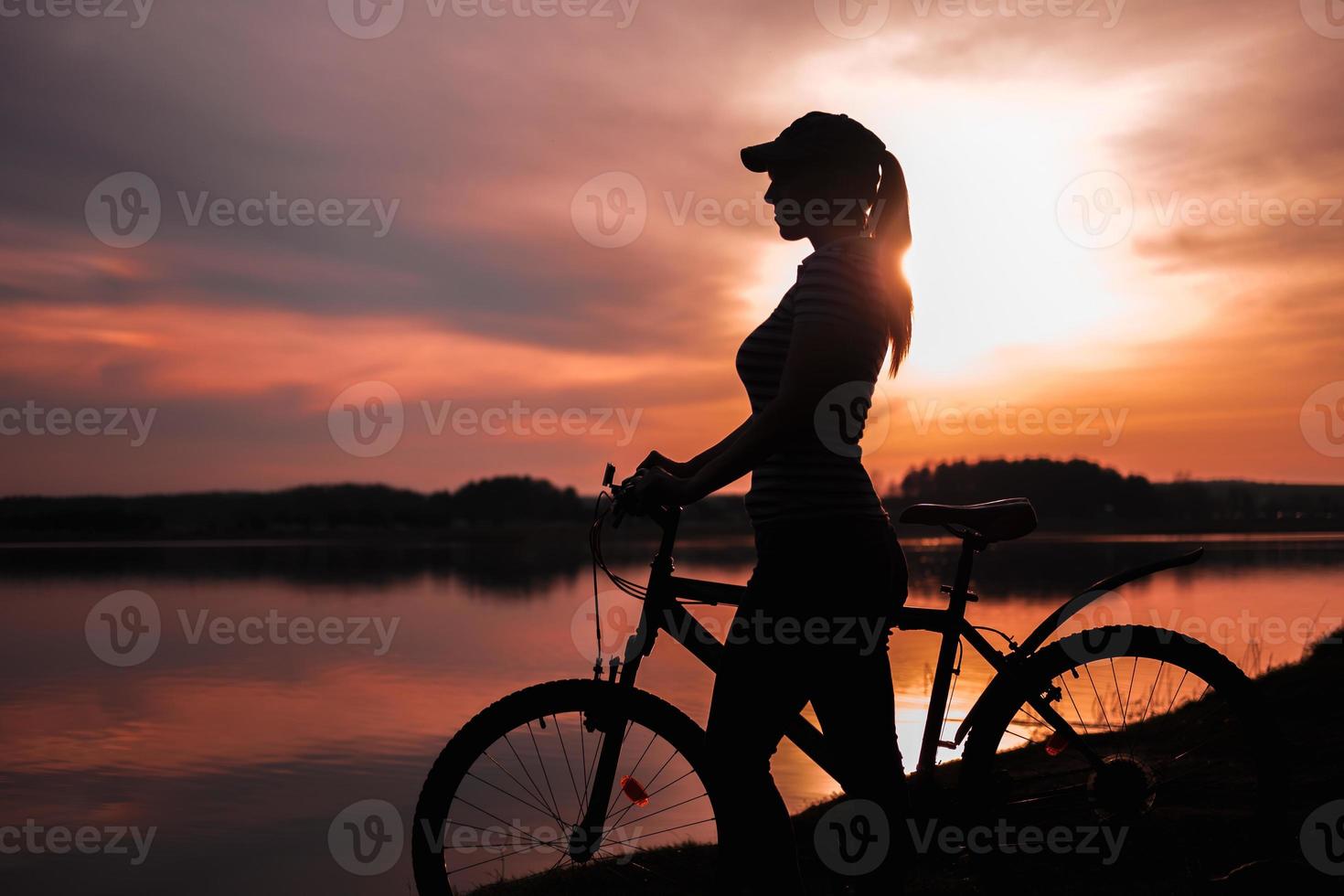 Summer silhouette landscape. Girl with a bicycle by the lake against the backdrop of the setting sun, the crimson sunset photo