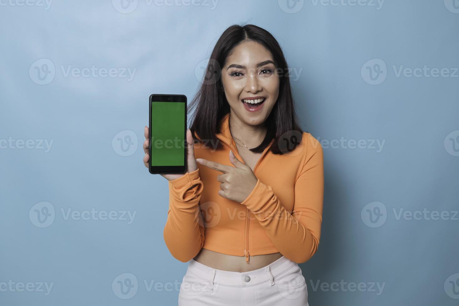 An excited young woman pointing at copy space on her smartphone in her hand, isolated on blue background photo