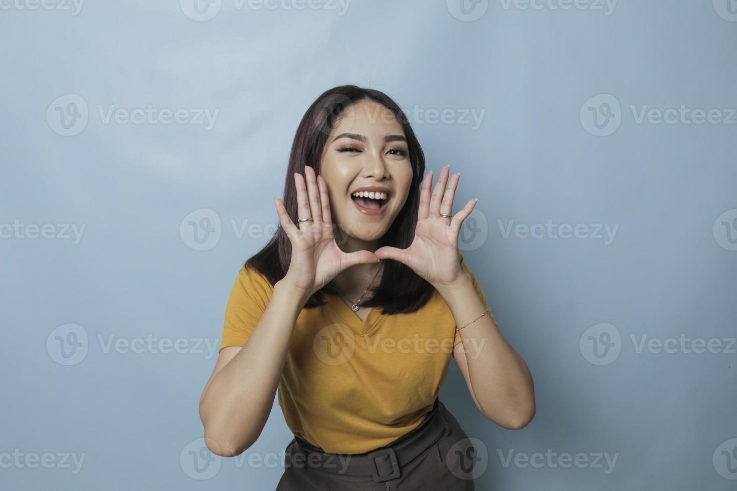 Surprised Asian woman reclines on her hands and shouting while looking at the camera over blue background photo