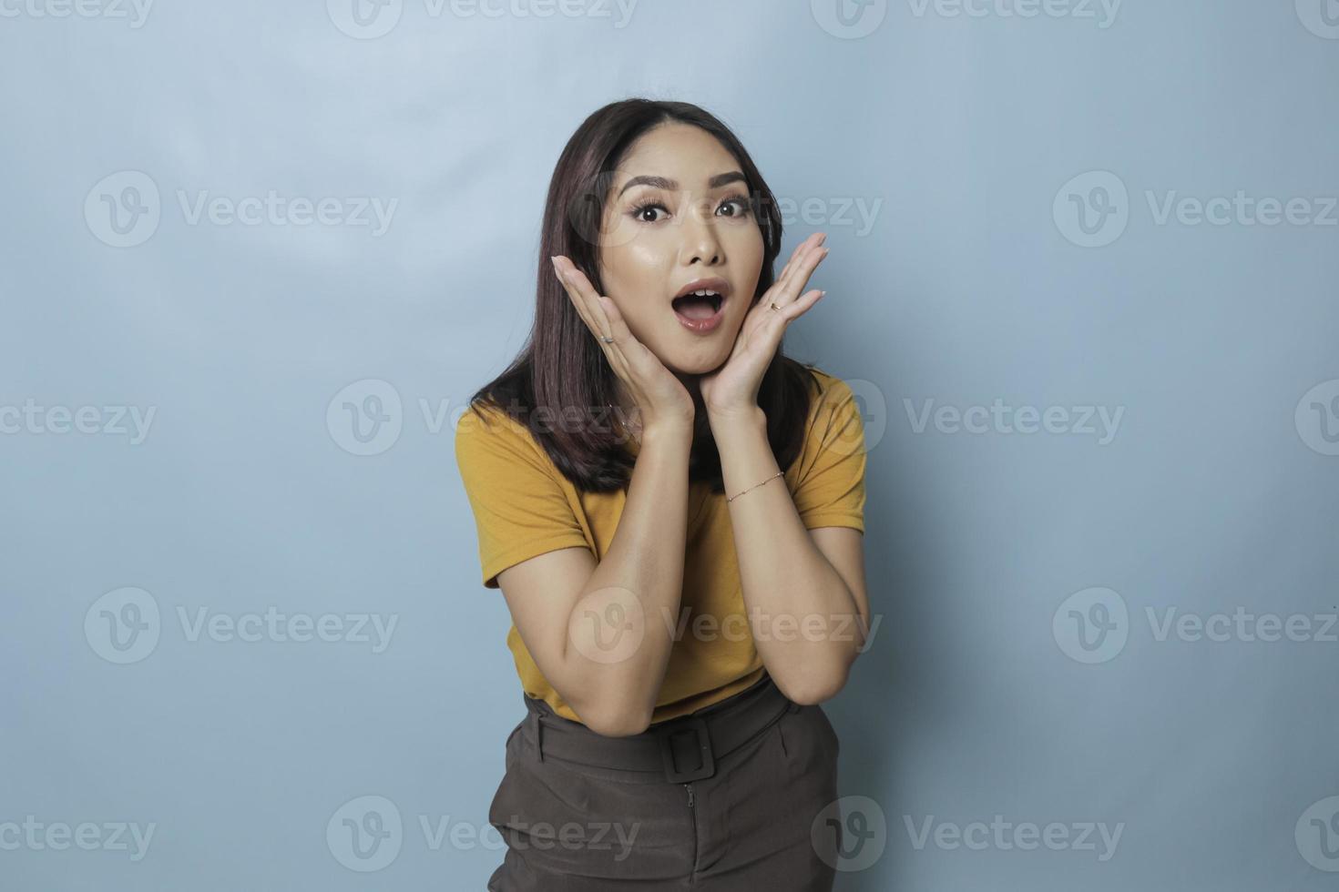 Surprised Asian woman reclines on her hands and shouting while looking at the camera over blue background photo