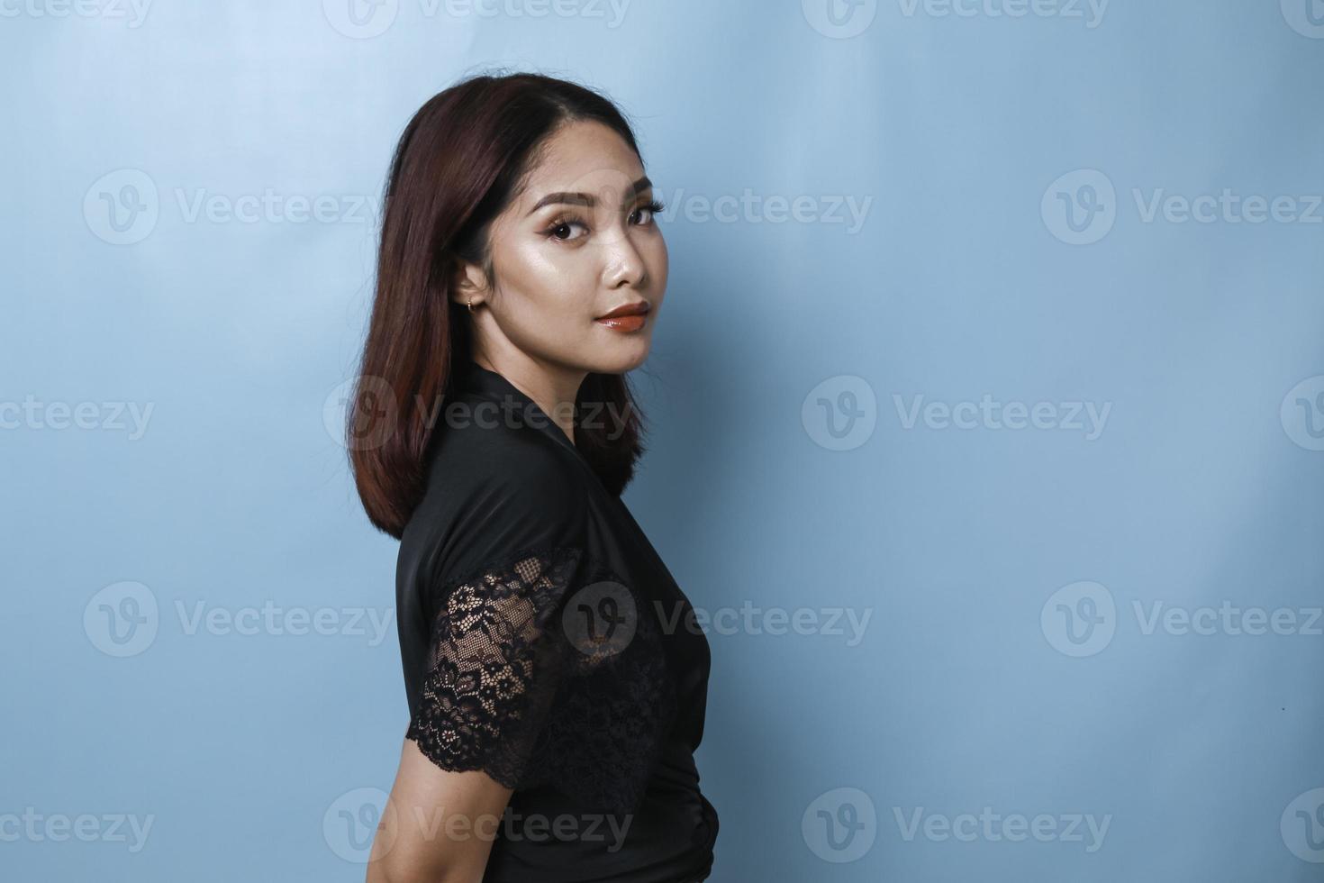 Side portrait of attractive Asian woman, wearing black shirt, smiling to the camera, isolated by blue background photo