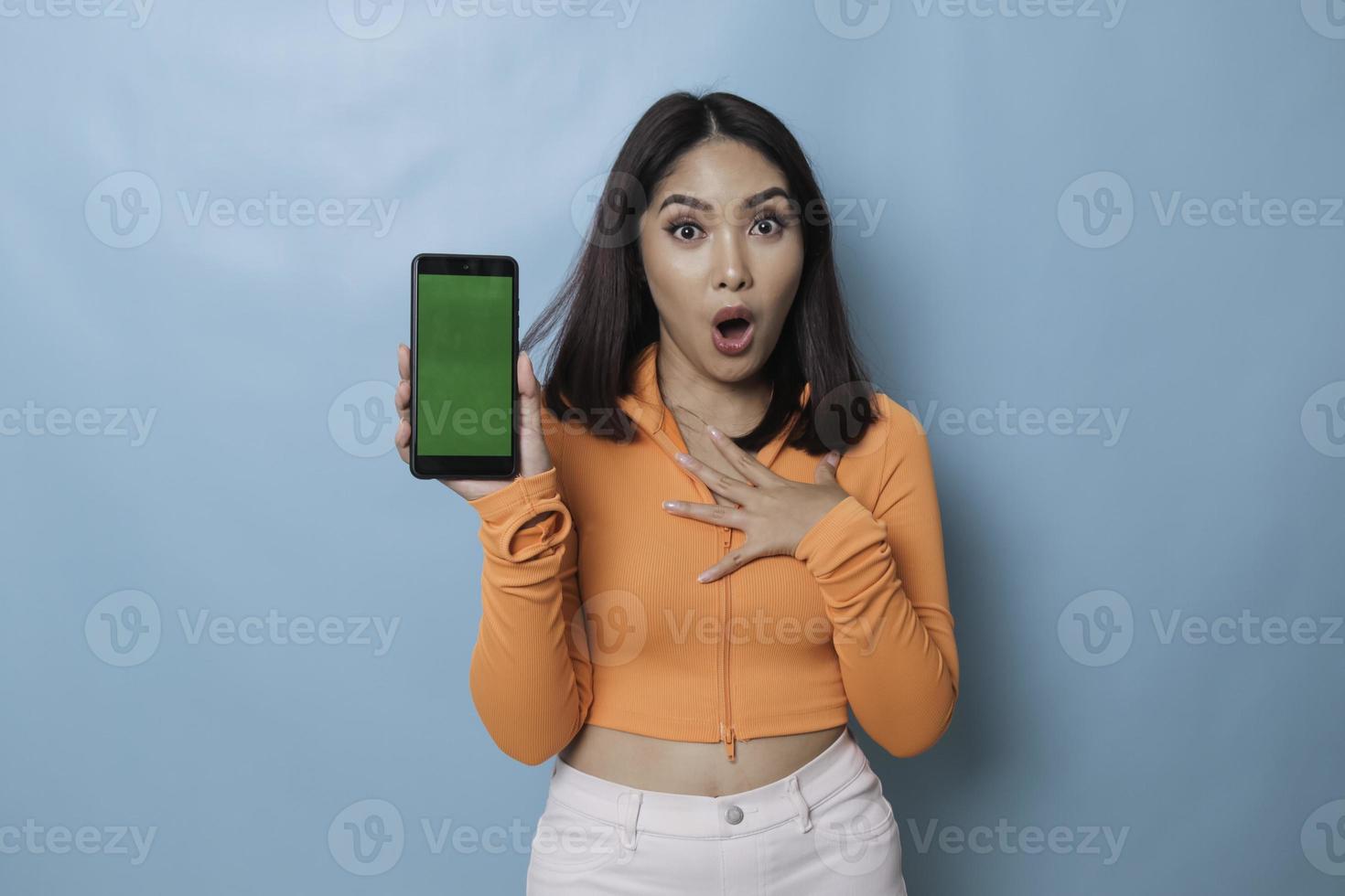 A surprised young woman pointing at copy space on her smartphone in her hand, isolated on blue background photo