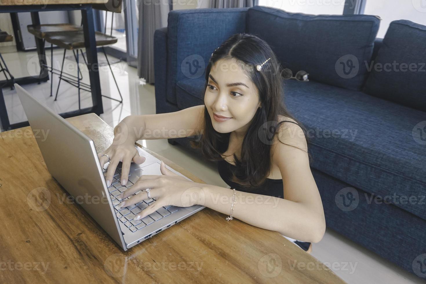 Young Asian woman spend her time at home sitting in the living room smiling and working on her laptop. photo