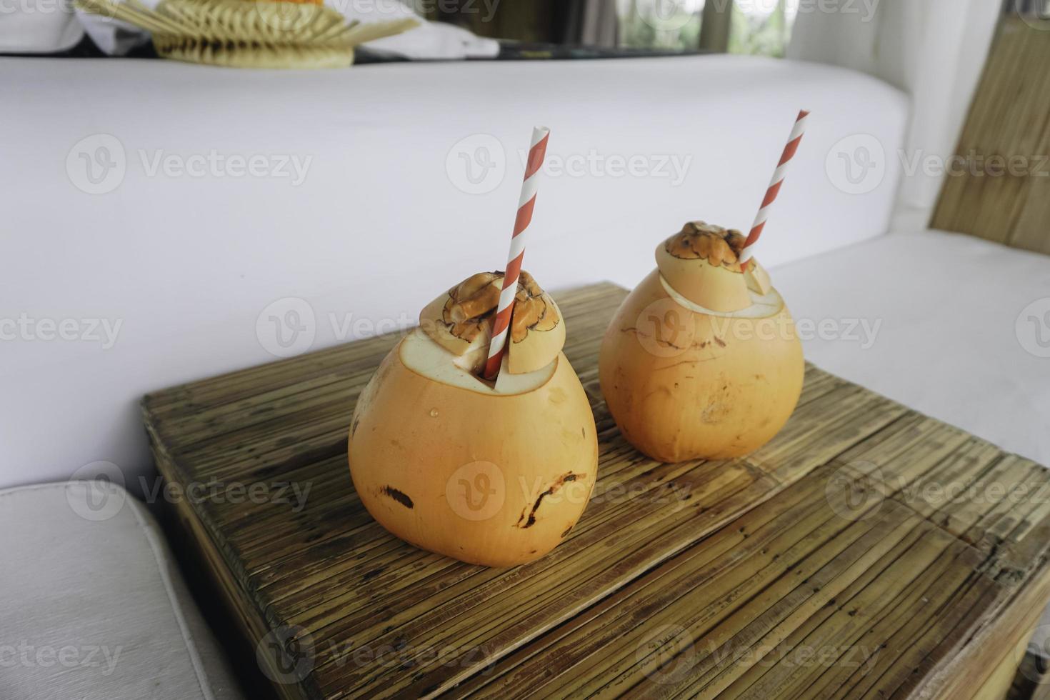 two coconut juices with paper straws placed on a wooden table photo