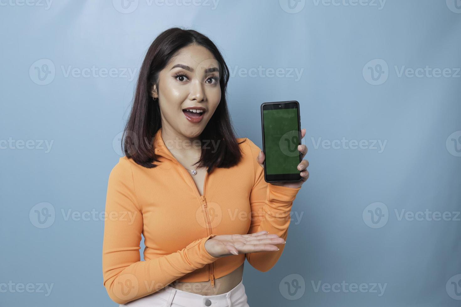 An excited young woman pointing at copy space on her smartphone in her hand, isolated on blue background photo