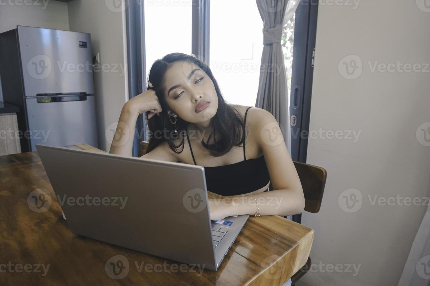 la joven asiática pasa su tiempo en casa sentada en el comedor frustrada y cansada trabajando en su computadora portátil. foto