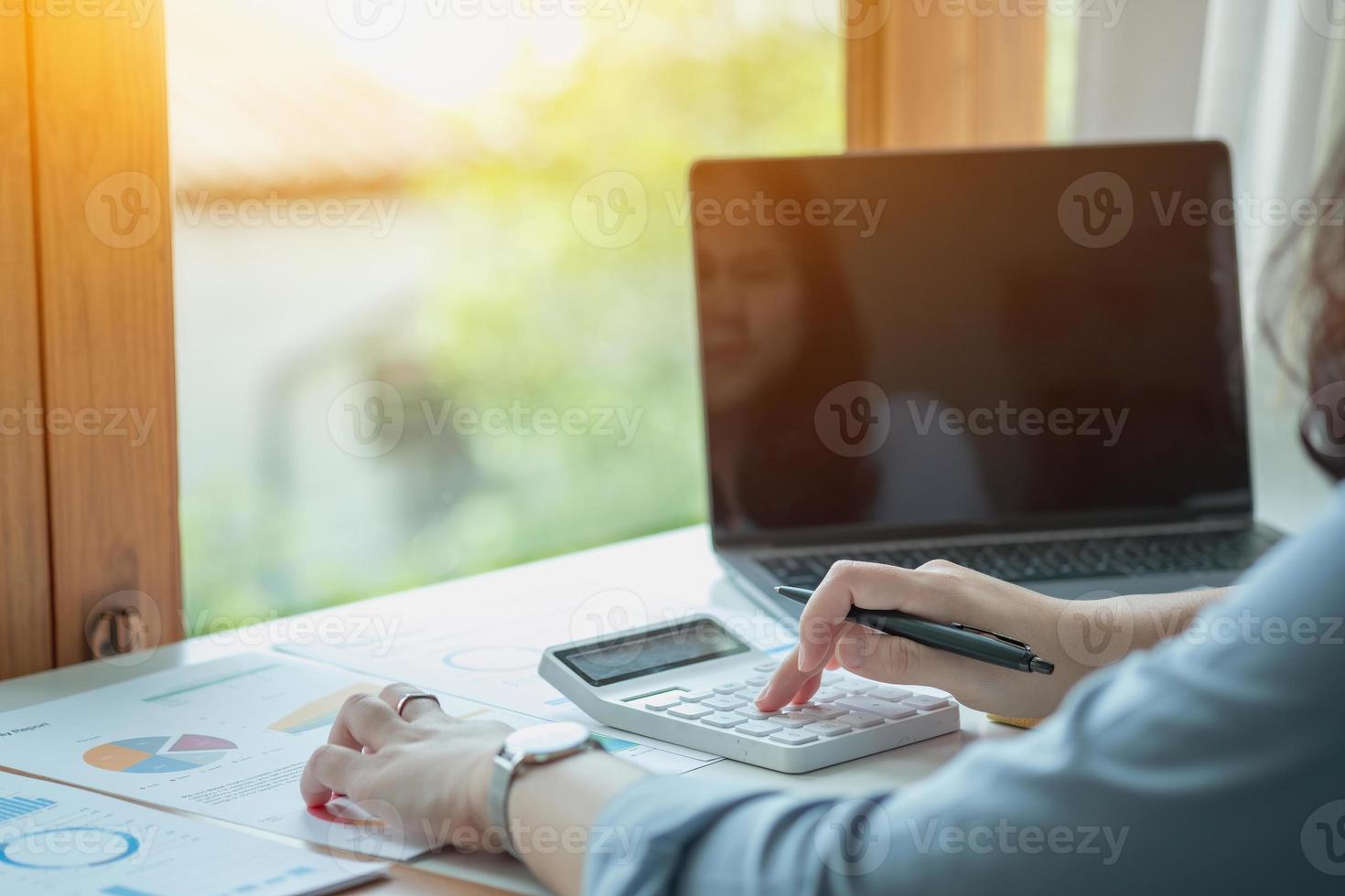 Portrait of a female accountant using a calculator and laptop to calculate balance using graphs for customers. photo