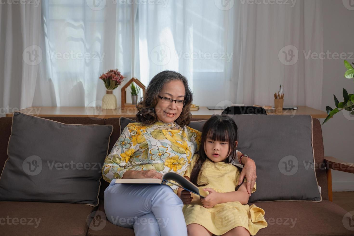 Portrait of an elderly woman and granddaughter reading a book to enhance reading skills and family activities. photo