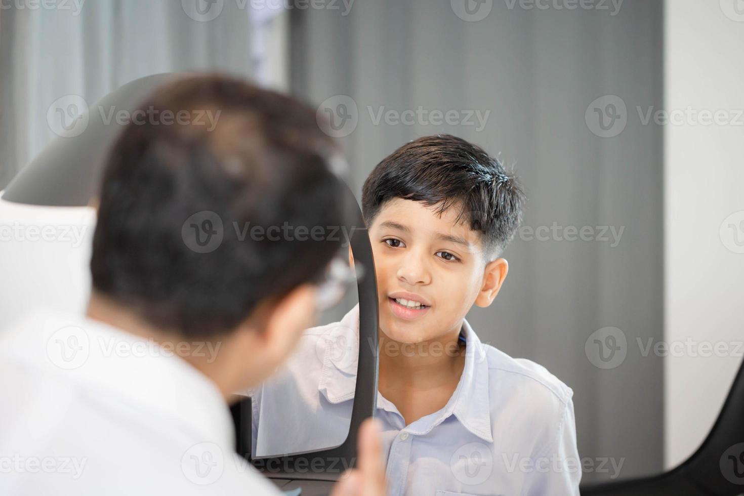 Boy doing eye test checking examination with autorefractor in optical shop, Optometrist doing sight testing for child patient, Eye doctor examinating kid patient photo