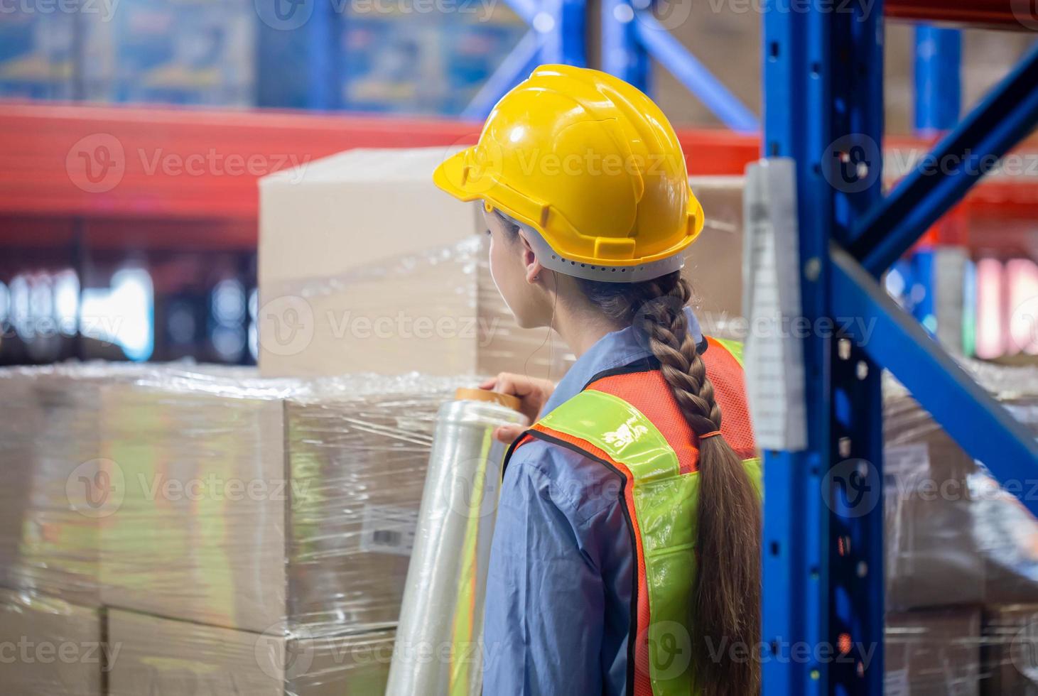 Female worker wrapping boxes in stretch film at warehouse, Worker wrapping stretch film parcel on pallet in factory warehouse photo