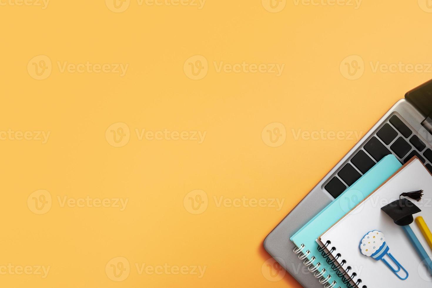 Colorful pencils with graduated cap and note on laptop on colored background. Copy space. Children work space top view, flat lay photo
