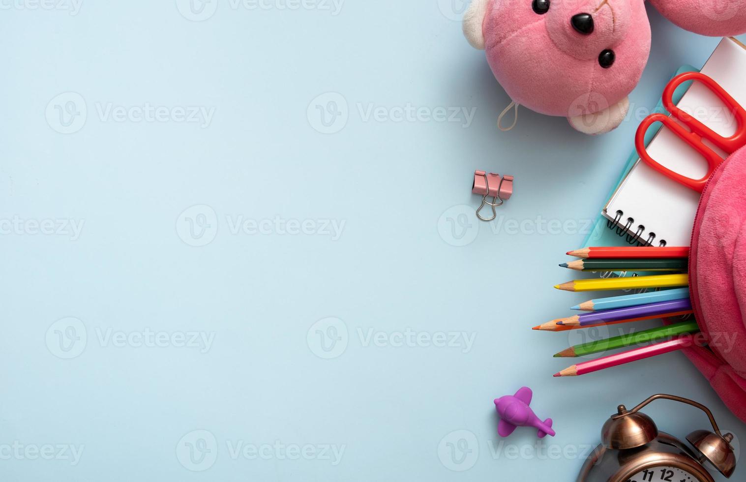 Teddy bear, alarm clock and stationary with backpack on colored background. Copy space. Top view, flat lay photo