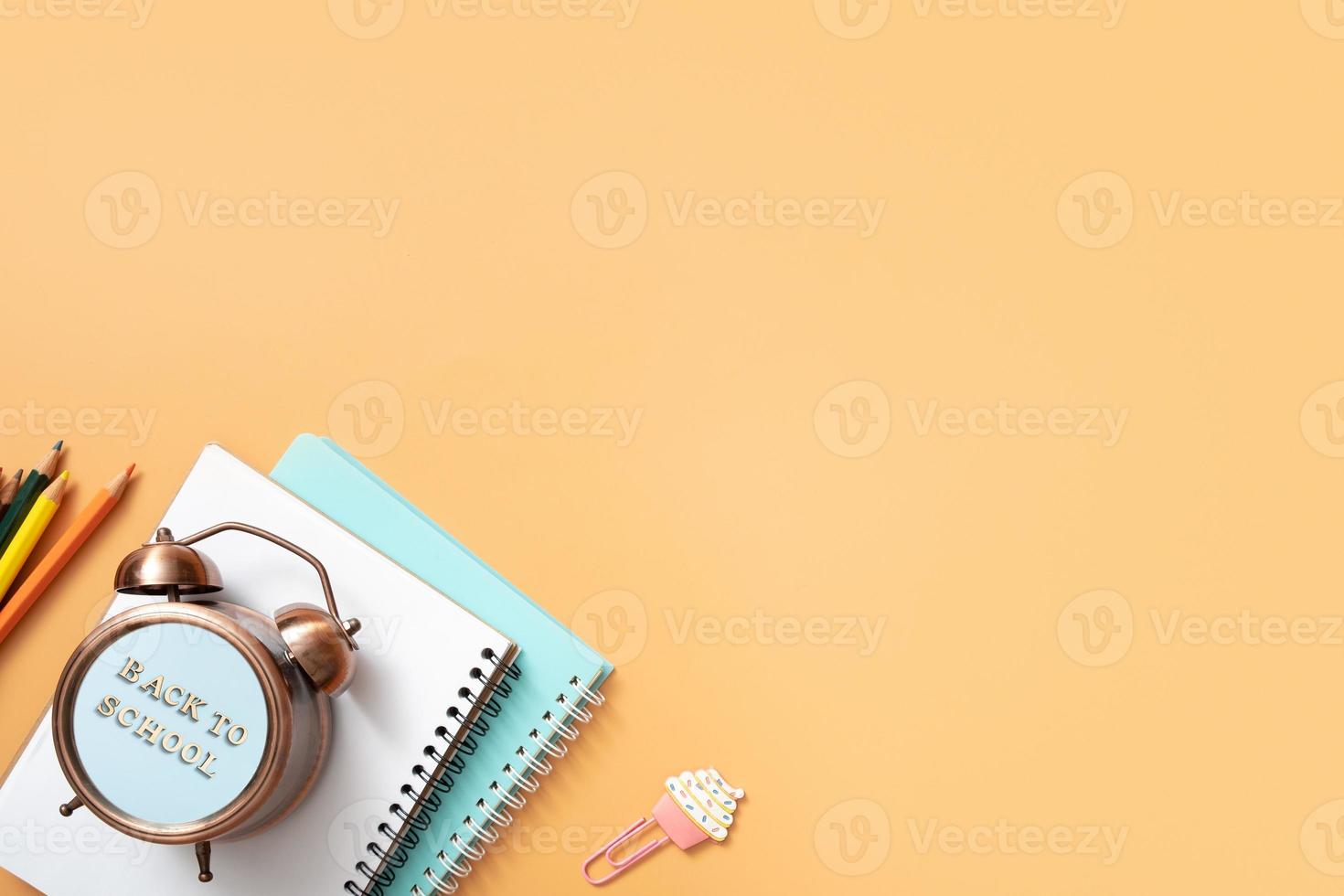 Notebooks, alarm clock with back to school text and stationary on colored background. Copy space. Kids work space top view, flat lay photo
