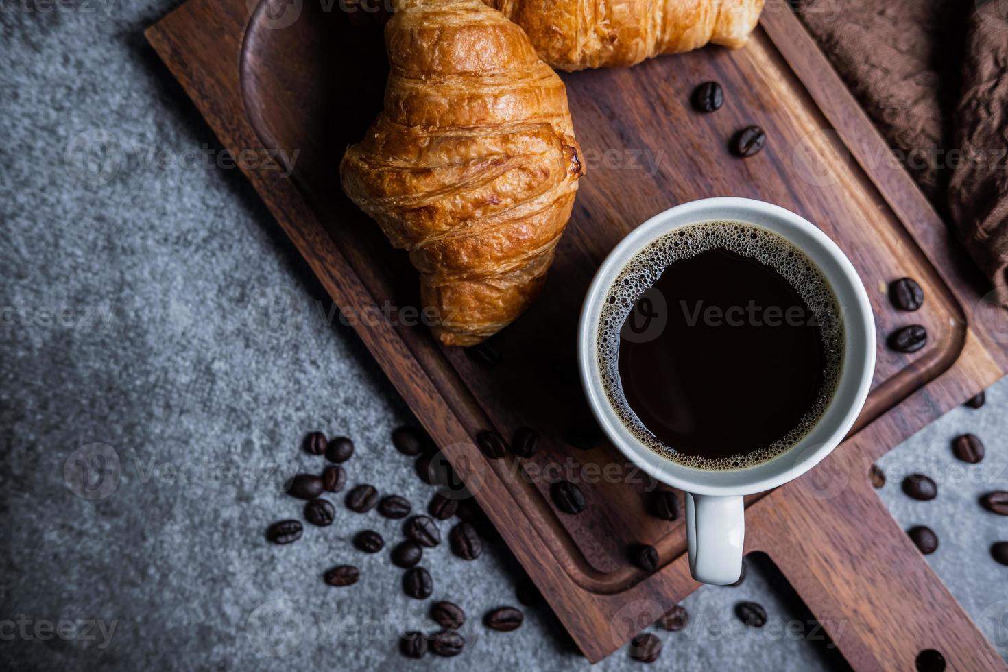 Breakfast with fresh croissants and cup of black coffee on wooden board photo