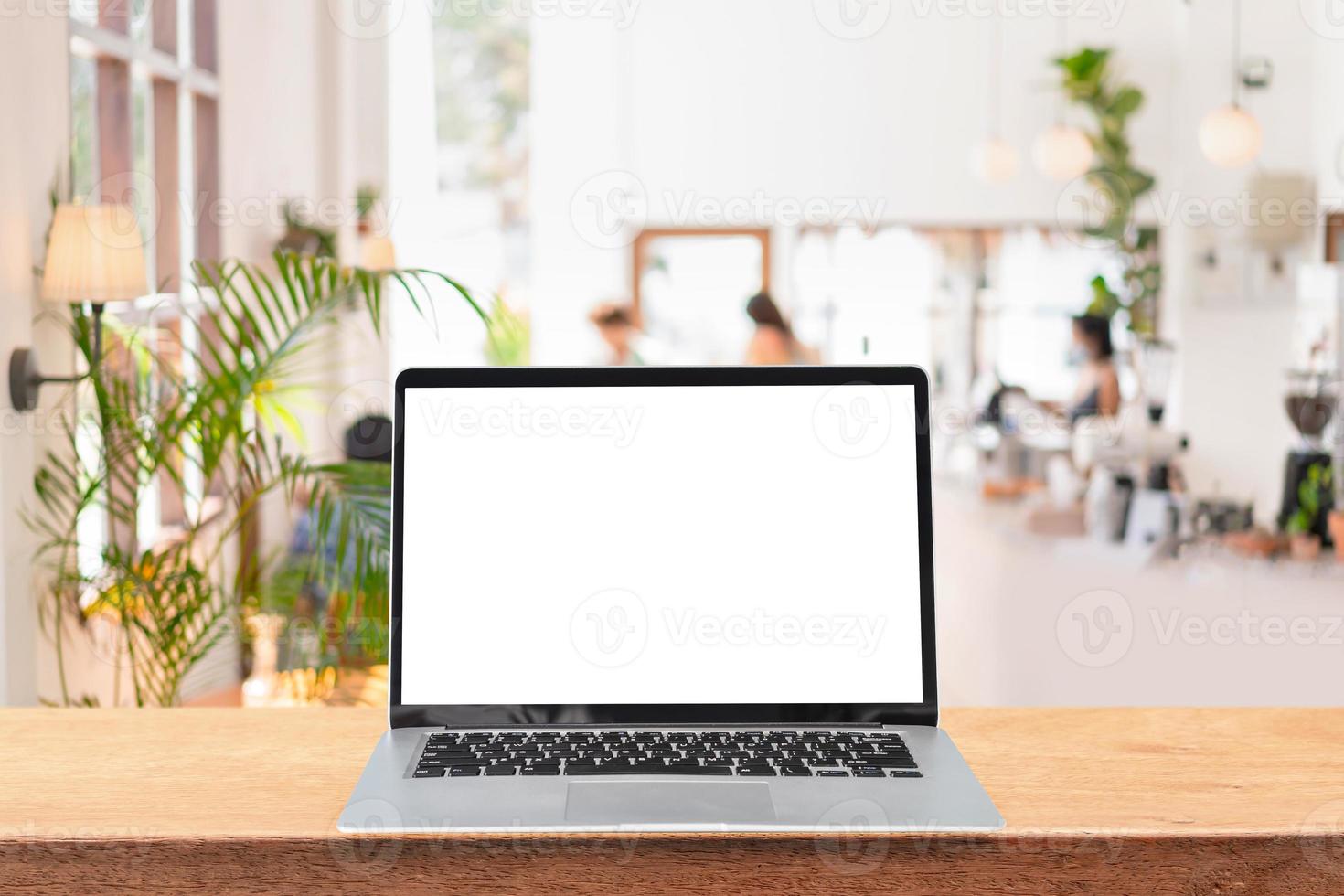 Empty screen laptop on a wooden table with blurry defocused restaurant interior and coffee shop background and copy space photo