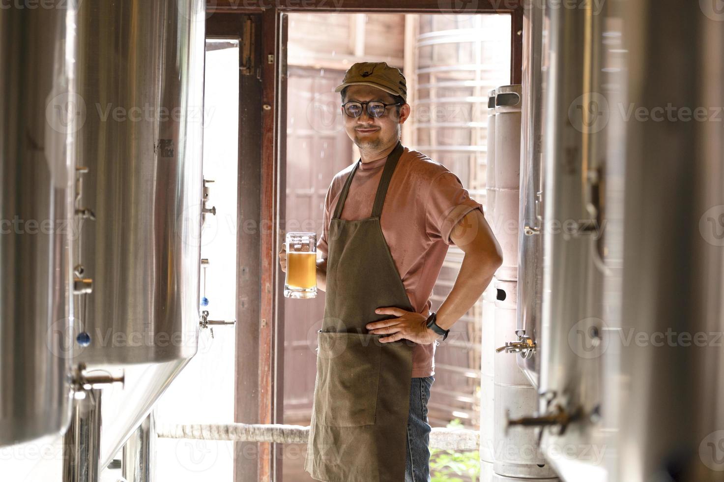 A young man works in a brewery and checks the quality of craft beer. The brewery owner tastes the best beers from Bach. A man's shortcut fills a glass of beer with photo