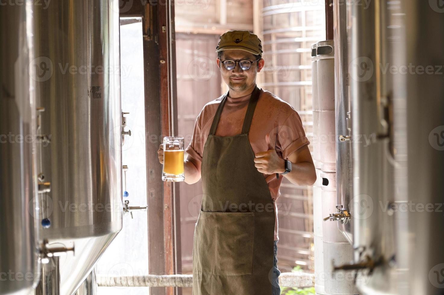 A young man works in a brewery and checks the quality of craft beer. The brewery owner tastes the best beers from Bach. A man's shortcut fills a glass of beer with photo