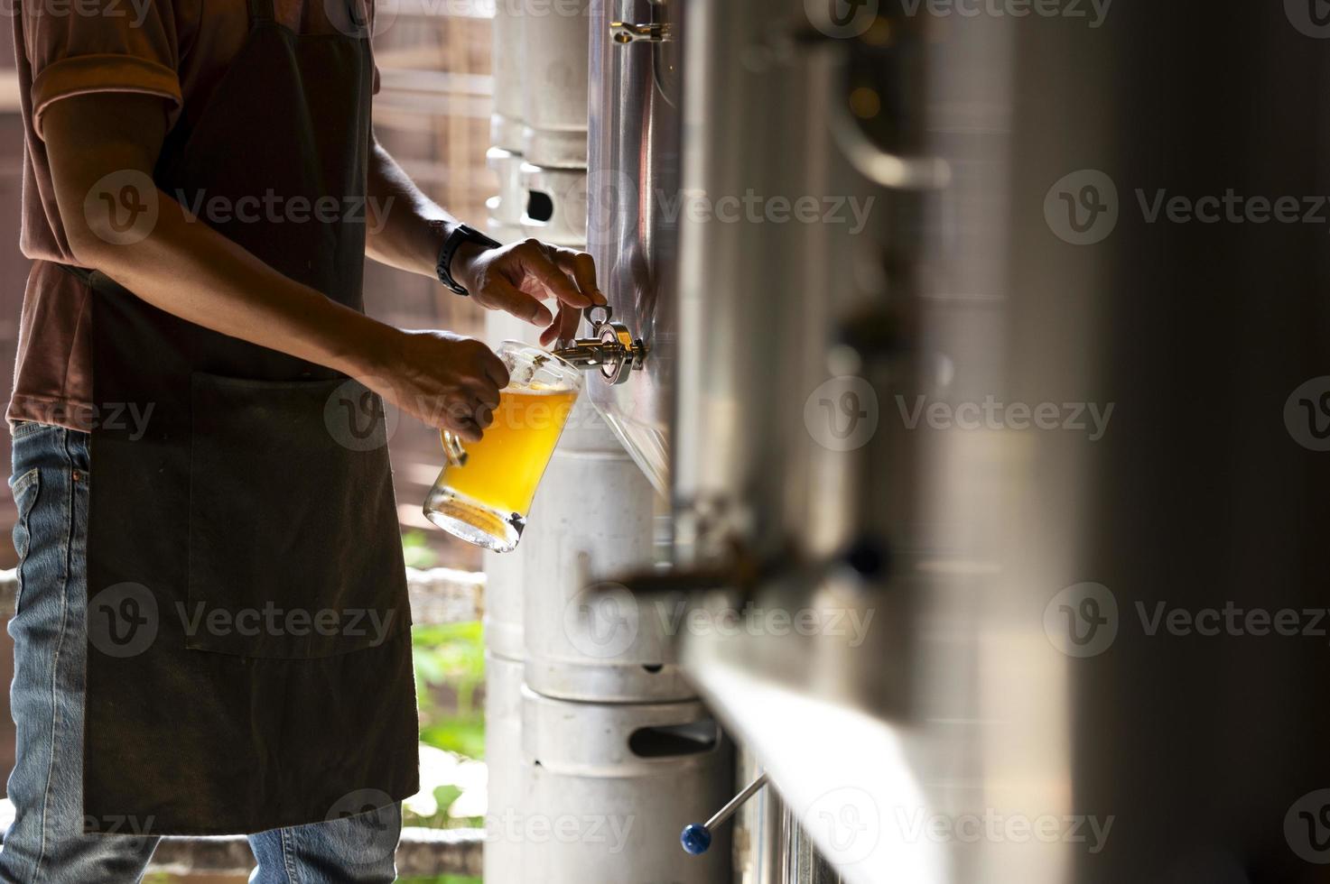 un joven trabaja en una cervecería y verifica la calidad de la cerveza artesanal. el dueño de la cervecería degusta las mejores cervezas de bach. el atajo de un hombre llena un vaso de cerveza con foto