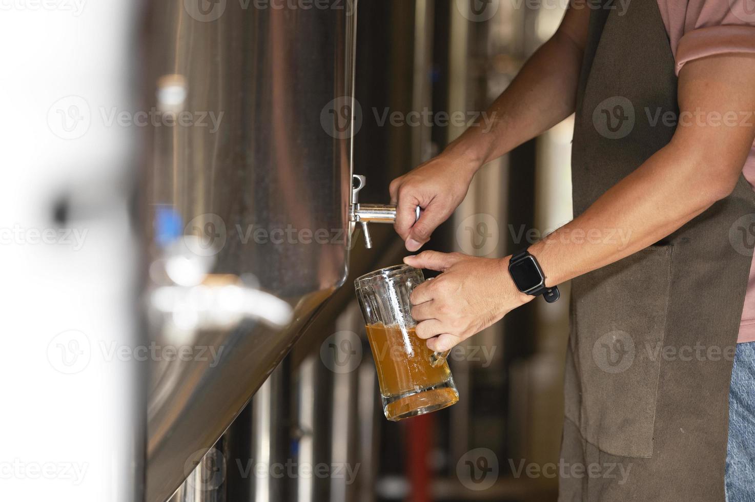 A young man works in a brewery and checks the quality of craft beer. The brewery owner tastes the best beers from Bach. A man's shortcut fills a glass of beer with photo