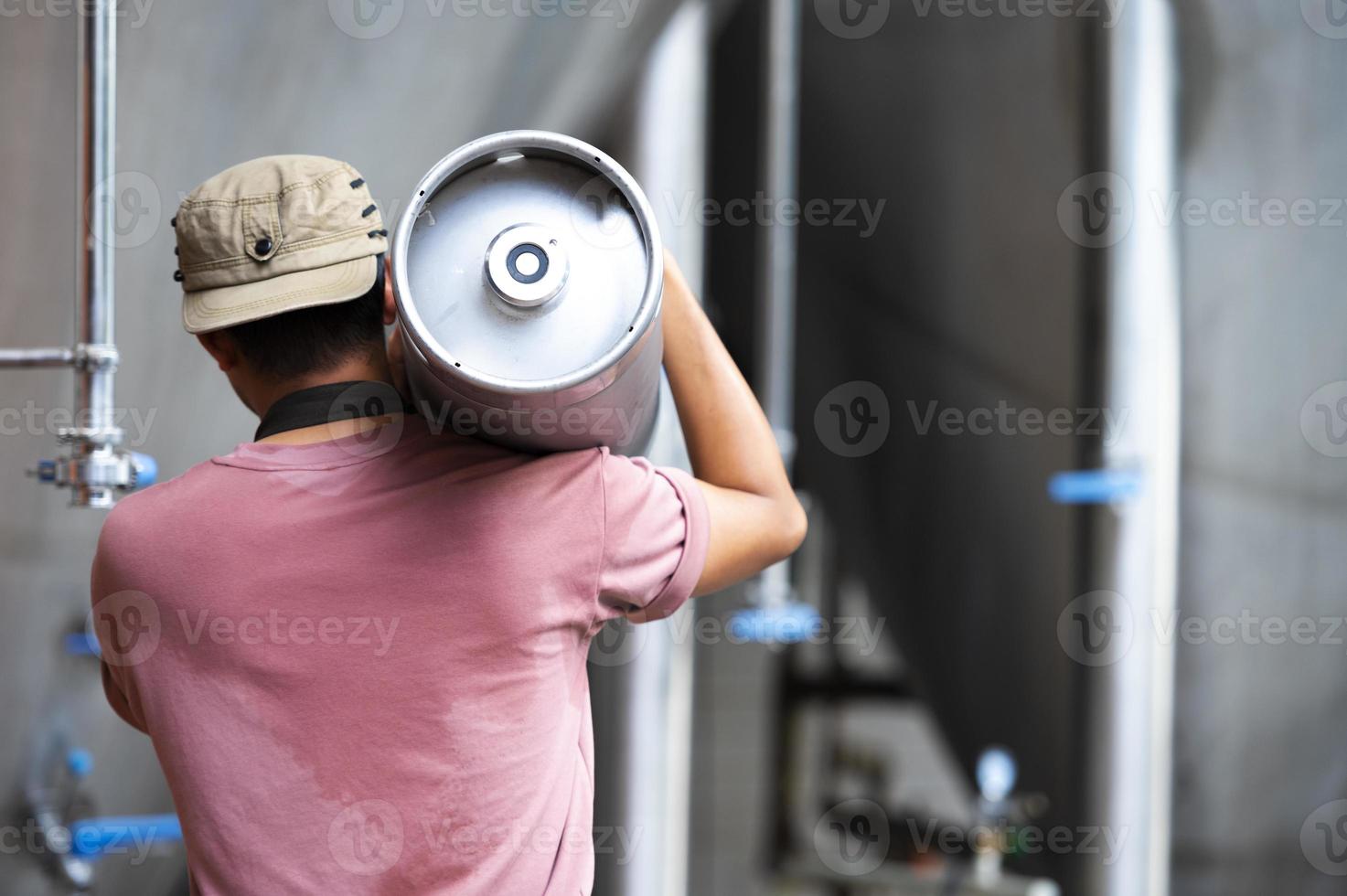 Young man in leather apron holding beer keg at modern brewery, craft brewery worker photo