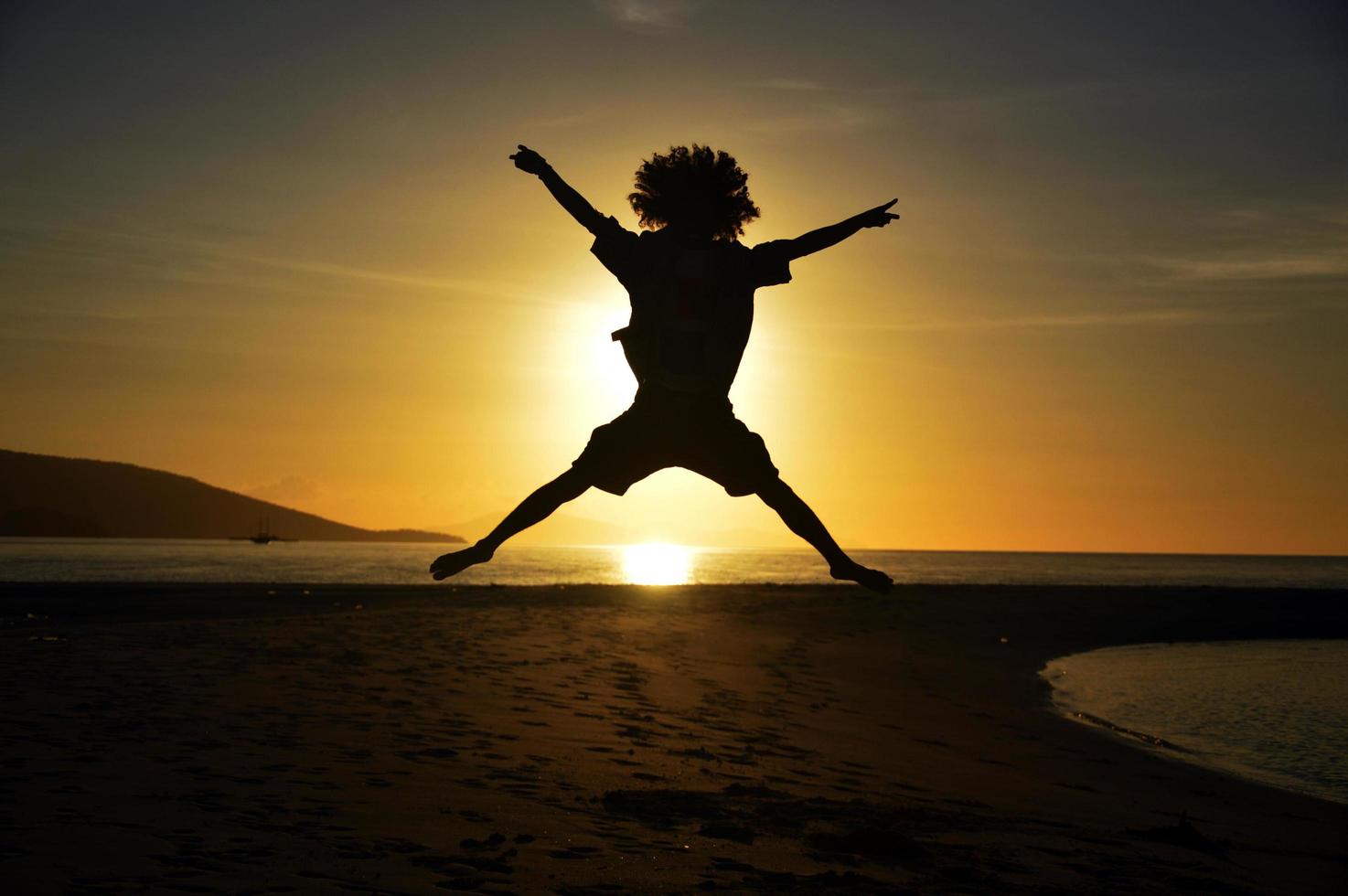 SILHOUETTE OF AN AFRO HAIRED MAN JUMPING WITH A SUNSET BACKGROUND photo