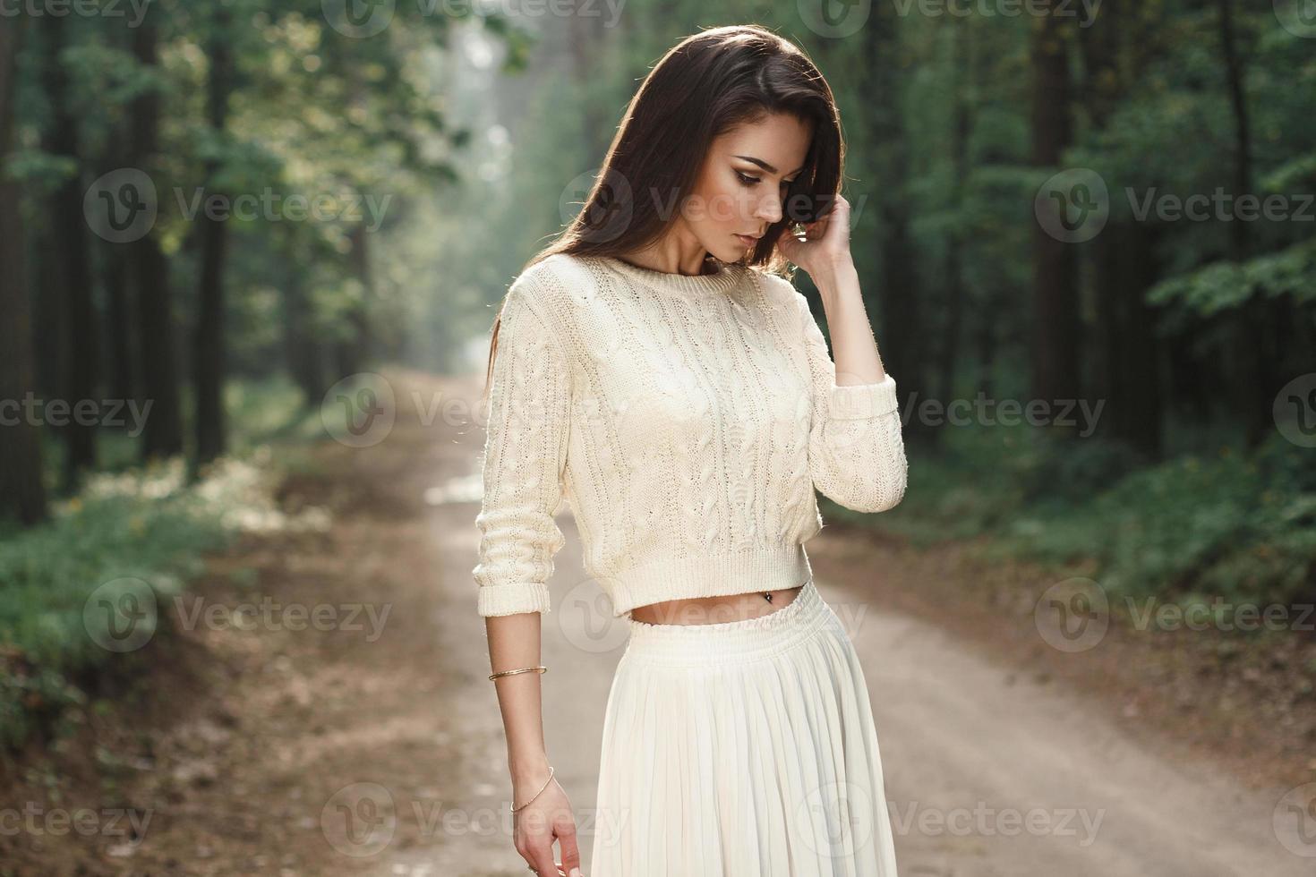 Portrait of a pretty woman in a white sweater on the road in the forest with fog. photo