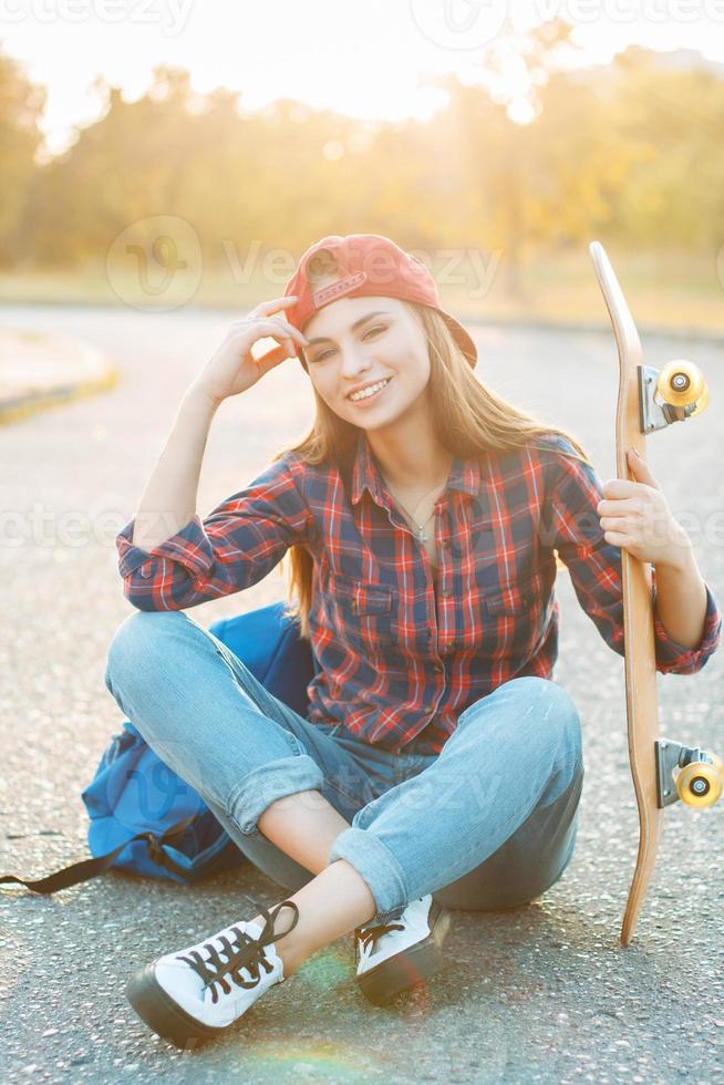 Portrait of a fun smiling young girl with skateboard and backpack at sunset. photo