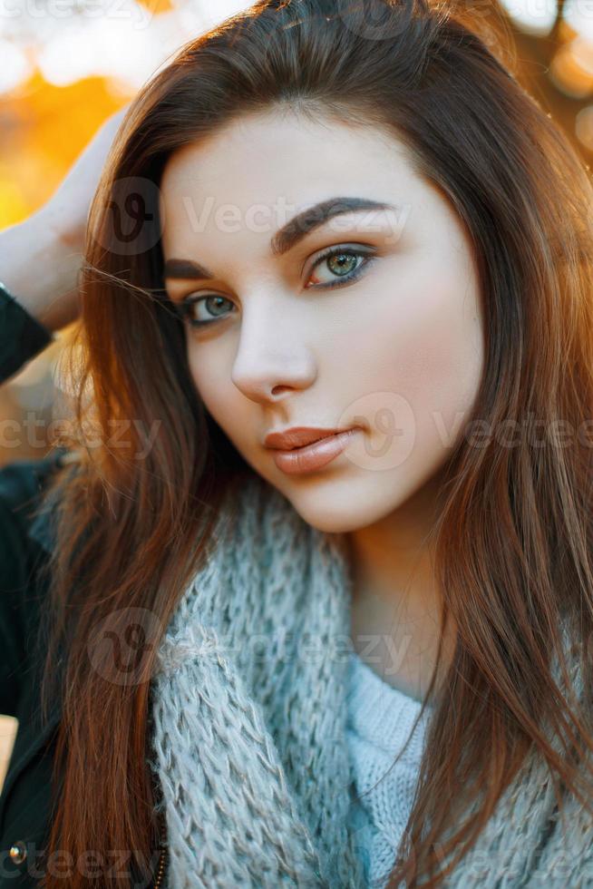 retrato de primer plano de una hermosa joven en una bufanda de punto gris en el fondo del parque de otoño foto