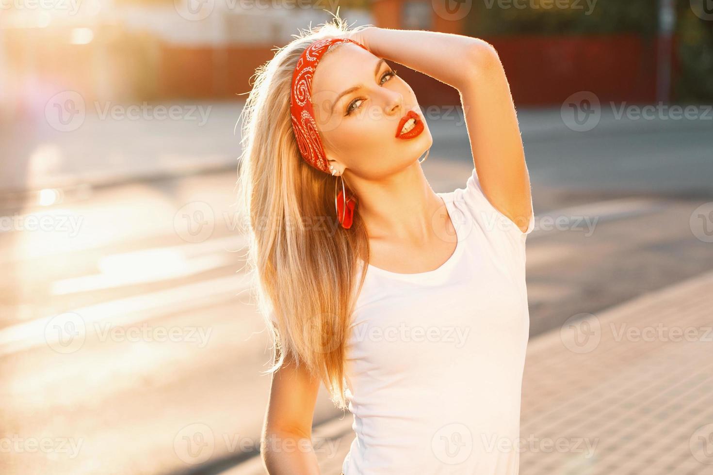 Portrait of a pretty hipster girl with red lips in white t-shirt on the street at sunset photo