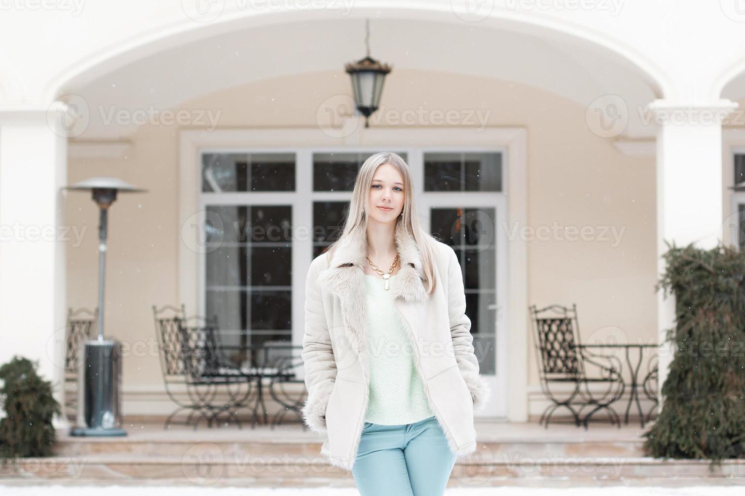 Beautiful girl in the winter jacket standing near the building photo