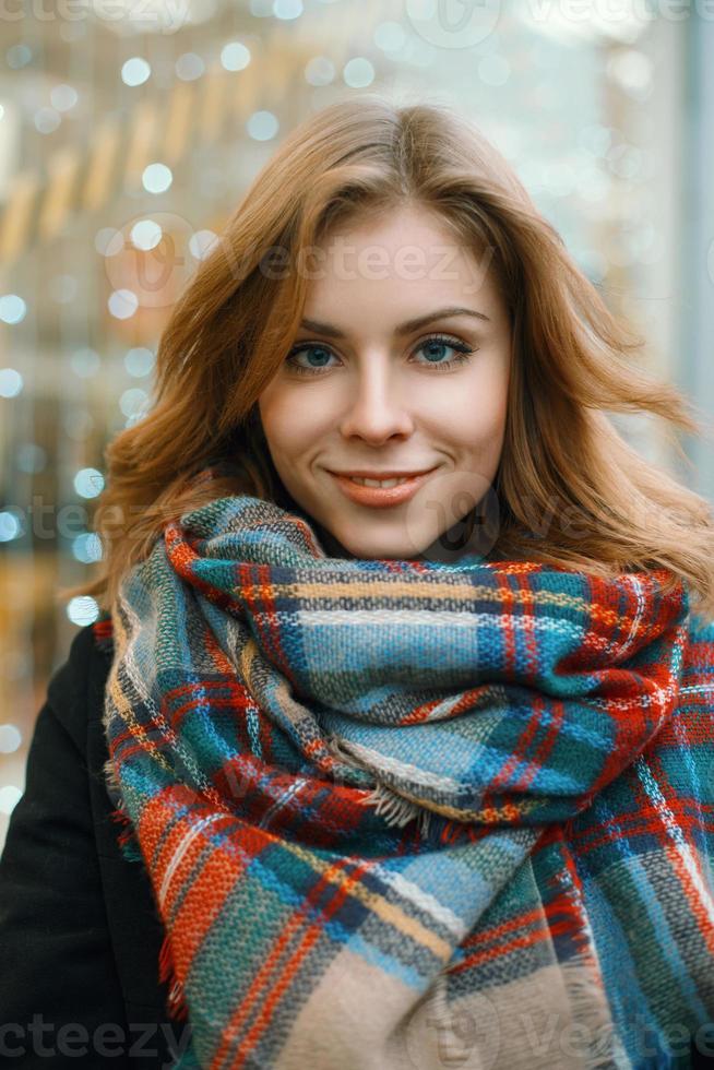 Close-up portrait of a beautiful woman in a stylish retro scarf and black coat on the background of showcases with lights photo