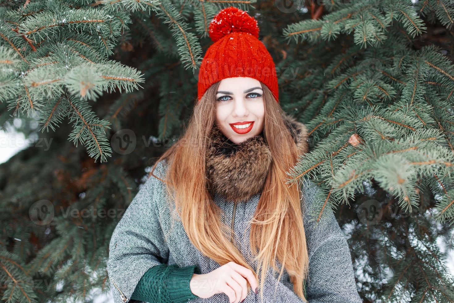 Hermosa mujer alegre en ropa elegante de invierno de pie cerca de abeto verde foto
