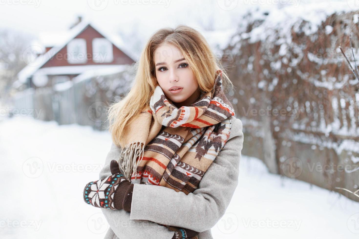 Beautiful woman with a vintage scarf and knitted mittens standing in the village near the fence photo