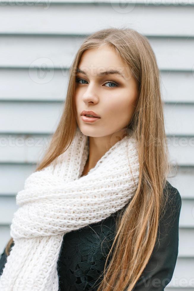 Young pretty girl with a white knitted scarf in autumn day on the background wooden wall photo